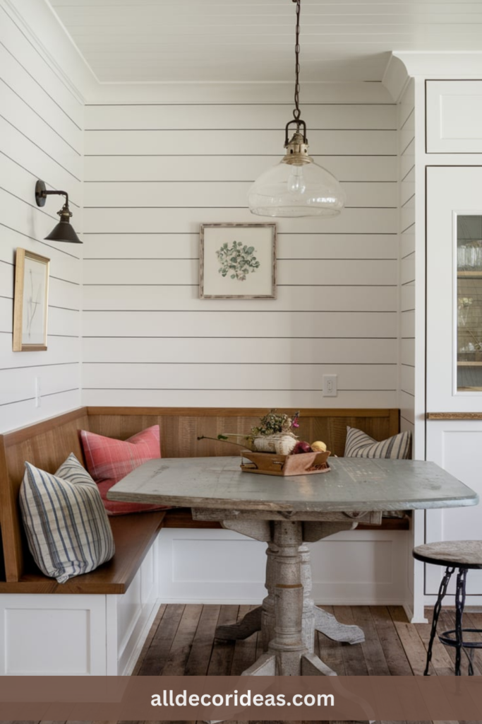 Rustic dining nook with built-in wooden bench, distressed table, shiplap walls, mismatched pillows, and vintage lighting.